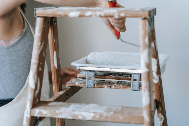 person in overalls using paint roller and ladder
