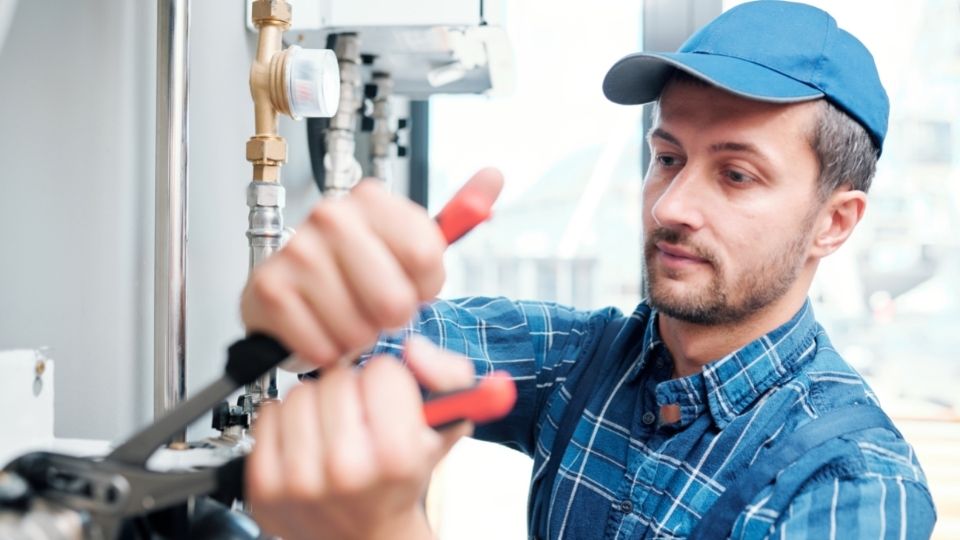 plumber in blue hat and shirt tightening bolt connecting two pipes