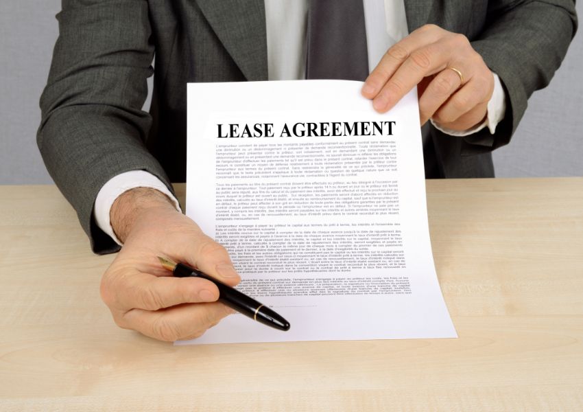 person holding up a lease agreement contract pointing to the signature line with a pen