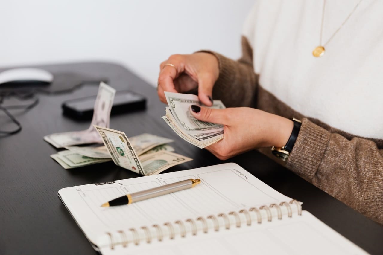 person counting money while sitting at their desk with a notebook in front of them