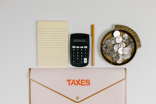 a notepad, calculator, coins and an envelope for taxes on a table