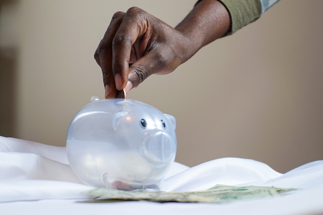hand dropping coins into a clear piggy bank