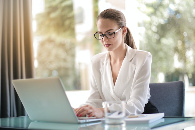 person in a white shirt and glasses working on a laptop
